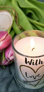 Romantic candle with pink tulips and heart decoration on a grey quilt.