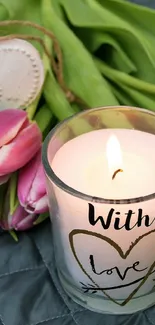 Candle with 'With Love' text beside pink tulips and heart decoration.