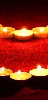 Heart-shaped candle arrangement on red fabric emits warm light.