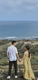 Couple holding hands overlooking ocean and landscape.