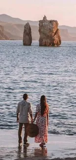 Couple gazing at sunset over the sea with rock formations.