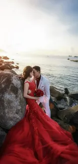 Couple embracing in red dress by a rocky beach during sunset.