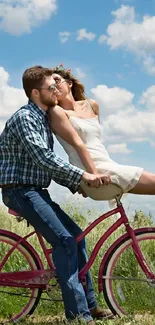 Couple riding a bicycle in a sunny field with blue skies.