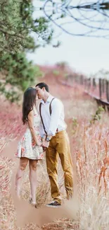 Romantic couple kissing in a field with pink grass and trees.