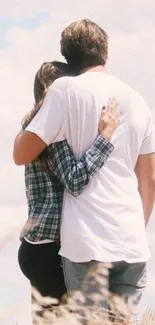 Romantic couple embraces in a natural setting with a bright, cloudy sky.