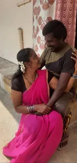 Romantic couple in pink saree sitting outdoors.