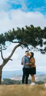 Couple embracing under a lone tree against a vibrant blue sky.