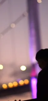 Silhouette by city bridge at twilight with soft colorful lights.