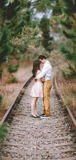 Couple embraces on a forest railway track.