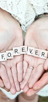 Hands holding Scrabble tiles spelling 'FOREVER' on grass.