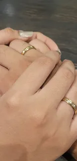 Hands with gold rings on a brown surface.