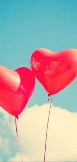 Two red heart-shaped balloons float in a bright blue sky with soft white clouds.