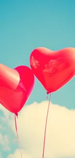 Two red heart balloons float in a bright blue sky.