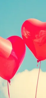 Two red heart-shaped balloons float in a bright blue sky.