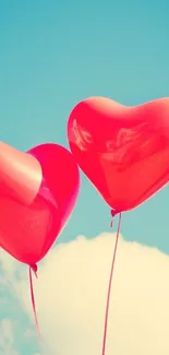 Two red heart-shaped balloons float in a clear blue sky.