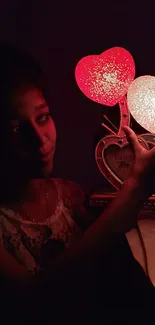 Person holding glowing heart-shaped lights in the dark.