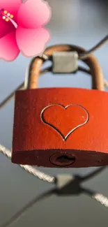 Red heart lock with pink flower on metal fence.