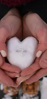 Hands hold a snow heart with a ring, capturing romance and winter charm.