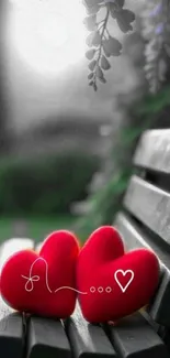 Two red plush hearts on a wooden park bench in nature.