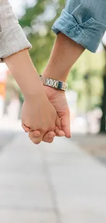 Couple romantically holding hands on a sunny pathway.