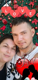 Romantic couple smiling in front of a festive Christmas tree with love hearts.