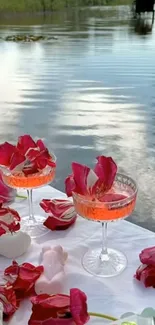 Lakeside picnic with red flowers and glassware at sunset.