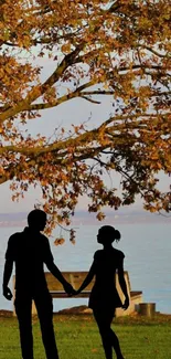 Romantic silhouette of a couple under an autumn tree by the lake.