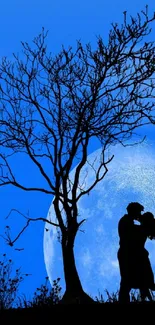 Silhouette of a couple kissing under a tree with a full moon backdrop.