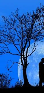 Silhouette of a couple kissing under a tree with a full moon in the background.