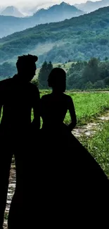 Silhouetted couple in front of a lush mountain landscape with a winding path.