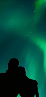 Silhouetted couple under the aurora borealis glow.