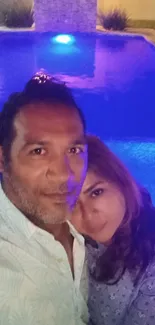 Couple enjoying a nighttime selfie by a blue-lit pool.