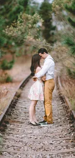 Romantic couple embracing on a railway track surrounded by greenery.