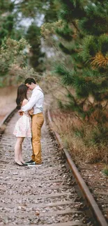 Romantic couple embracing on a scenic railroad with lush greenery.