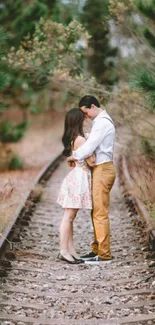 A couple embraces on a railway, surrounded by nature.