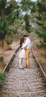 Couple embracing on railway tracks with trees in the background.