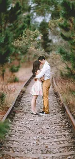 A couple embraces on railway tracks amidst green trees.