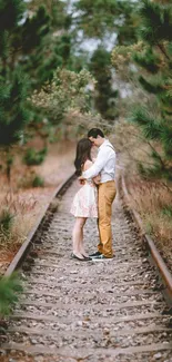 Couple embracing on forest railway with lush greenery.