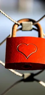 Red heart-shaped lock on wire fence, symbolizing love.