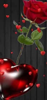 Red rose and glass heart on black wood background.