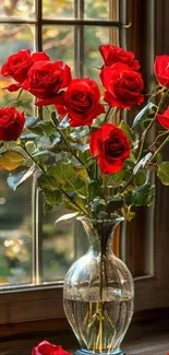 Bouquet of red roses in a glass vase by a window.