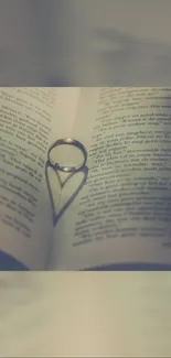 Ring creates heart shadow on book pages, romantic mobile wallpaper.