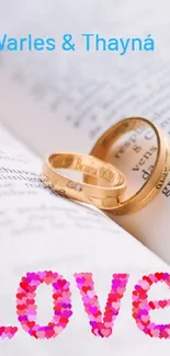 Gold rings on open book with 'Love' text in pink, ideal for romantic themes.