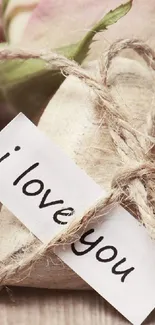 Romantic pink roses and heart with an 'I love you' note on wooden background.