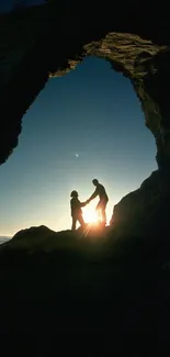 Silhouette of a couple under a rocky arch at sunset on the beach.