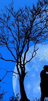 Silhouette of couple kissing under a moonlit blue sky and tree.