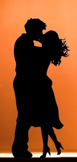 Silhouette of a couple kissing at sunset on an orange background.