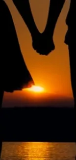 Silhouette of a couple holding hands at sunset by the water.