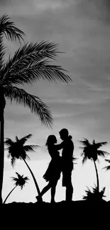 Couple silhouette under palm trees at sunset.