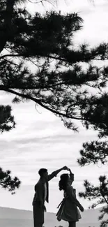 Silhouette of a couple dancing under trees in a scenic landscape.